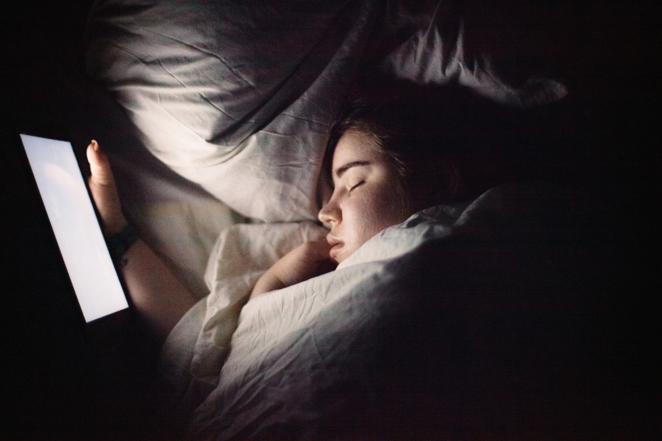 Jonge vrouw houdt een digitale tablet vast terwijl ze 's nachts in bed slaapt