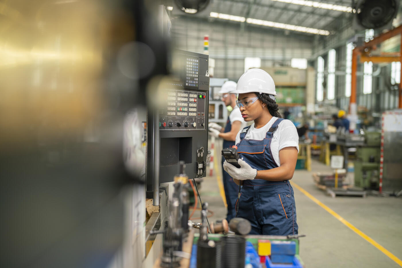 Female apprentice engineer working with CNC machine in factory