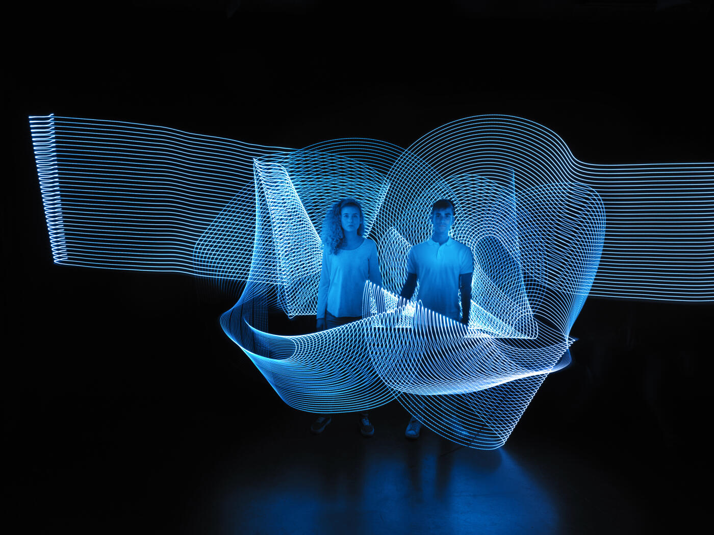 young couple holding hands with lighttrace arround them, looking towards the camera