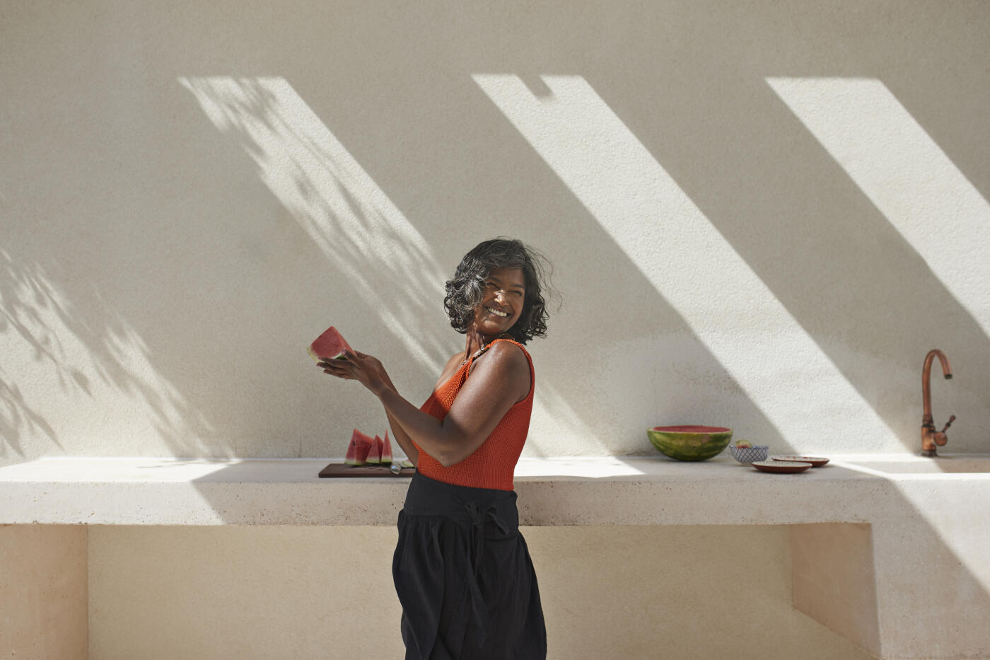 Happy mature woman with fresh slice of watermelon standing by counter