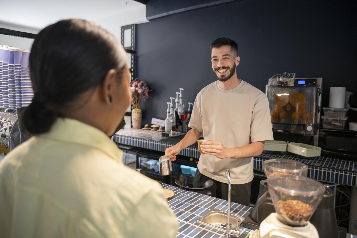 Young man with beard working in coffee shop serving woman with cheerful expression, Abha, Saudi Arabia