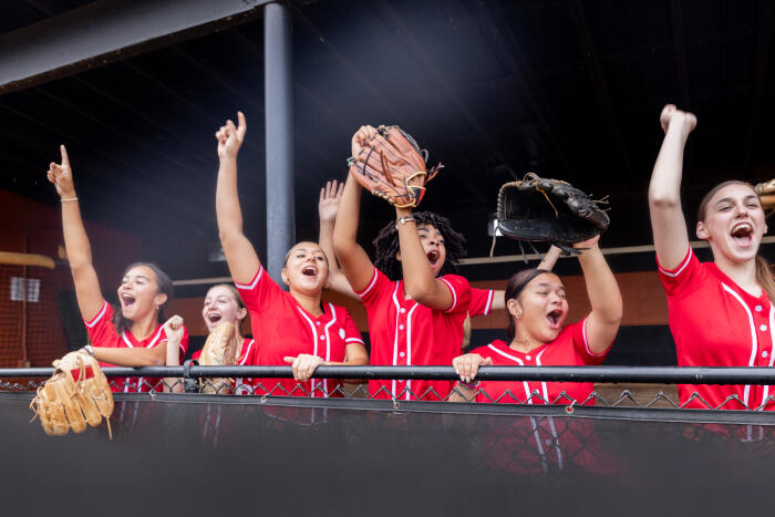 Diverse teenage softball players cheer after teammates scores homerun during game