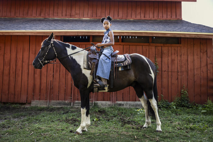 Portrait of young girl sitting on horse in front of barn