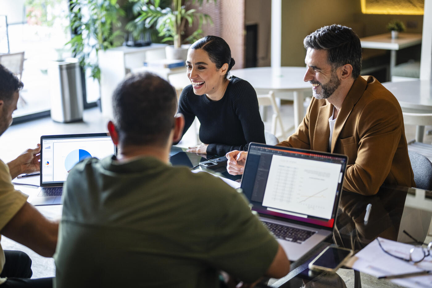 Iranian businesswoman and male co-workers sitting at table with laptops, brainstorming ideas, enthusiasm, energy, positivity