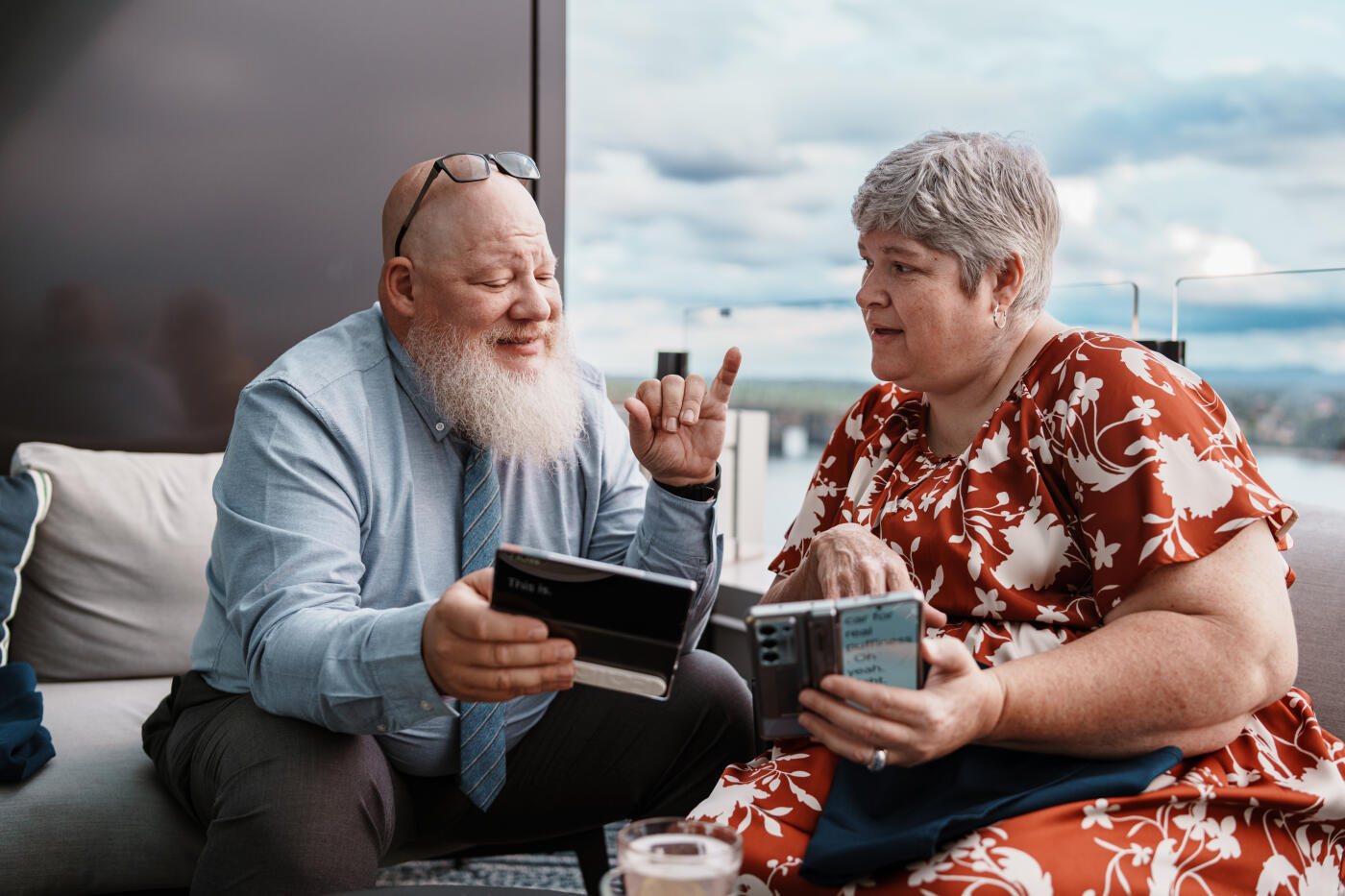 A Deaf mature adult couple communicate using sign language and a transcription mobile app on their smart phones while having drinks before dinner on the rooftop patio of an upscale restaurant.
