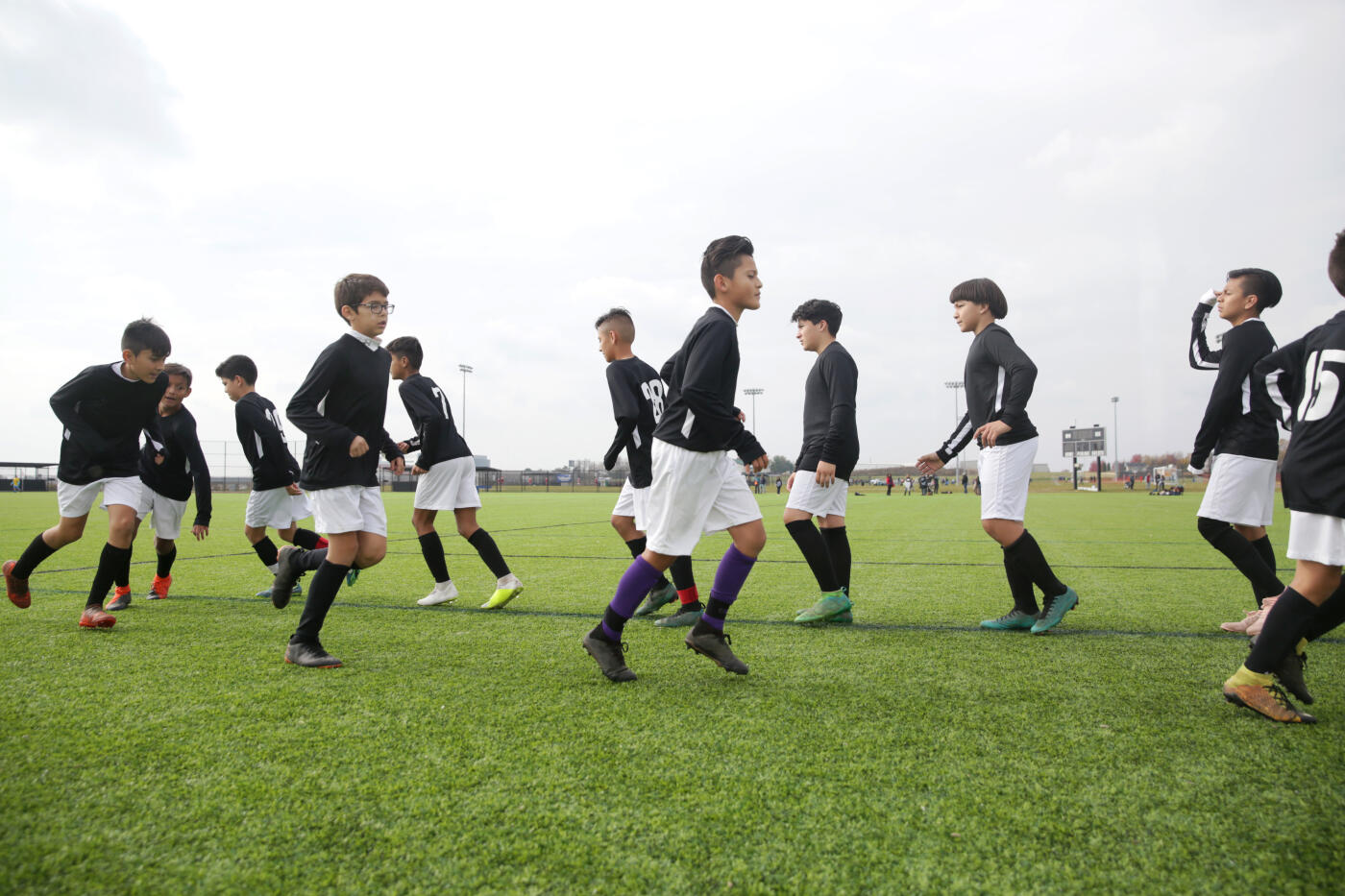 A group of teenage Latino soccer players do drills in their team uniforms on an outdoor soccer field.