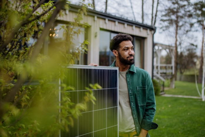 Portrait of young man with solar panel standing in front of house.