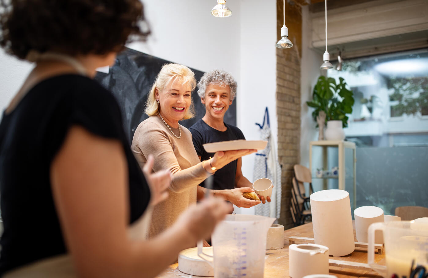 Senior woman looking happy after making a ceramic plate at art class. People making porcelain products at pottery workshop with teacher in front.
