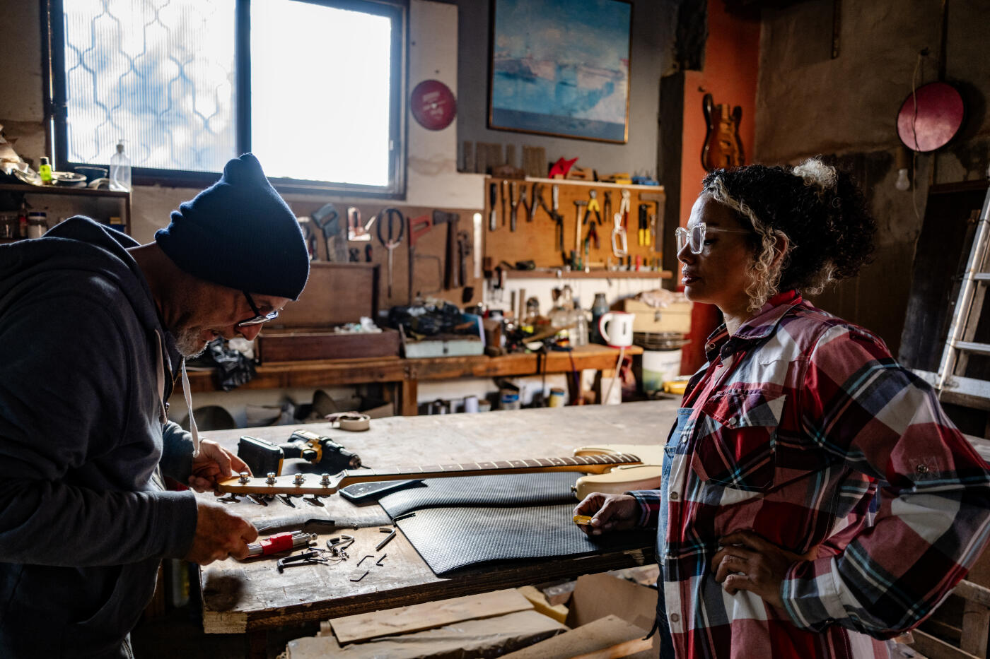 A middle-aged Latina luthier and a man with glasses repair a musical instrument in their studio.