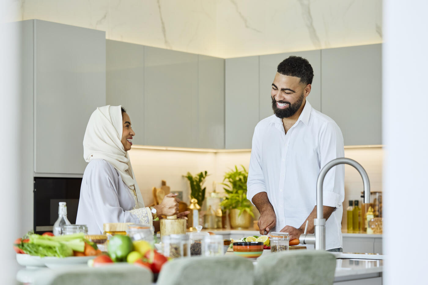 Happy man helping woman in abaya while preparing food at home. Saudi couple working together in kitchen. She is using mortar and hustle.