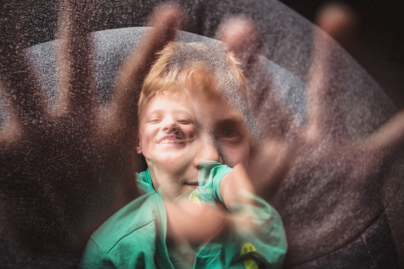 Smiling boy reaches out towards camera with a big smile on his face while double exposed with a calm portrait.