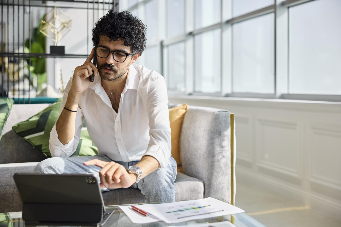 Businessman talking on smart phone while working at office. Male entrepreneur is discussing reports on call. He is also looking at digital tablet.