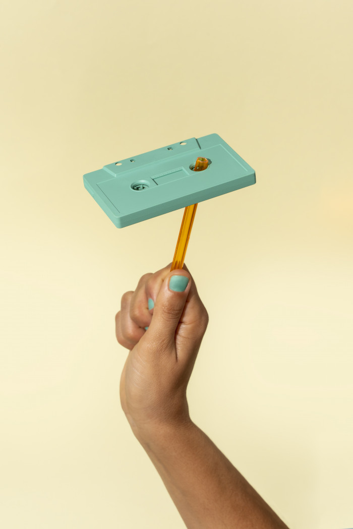 Hand Rewinding A Green Cassette Tape On Yellow Background