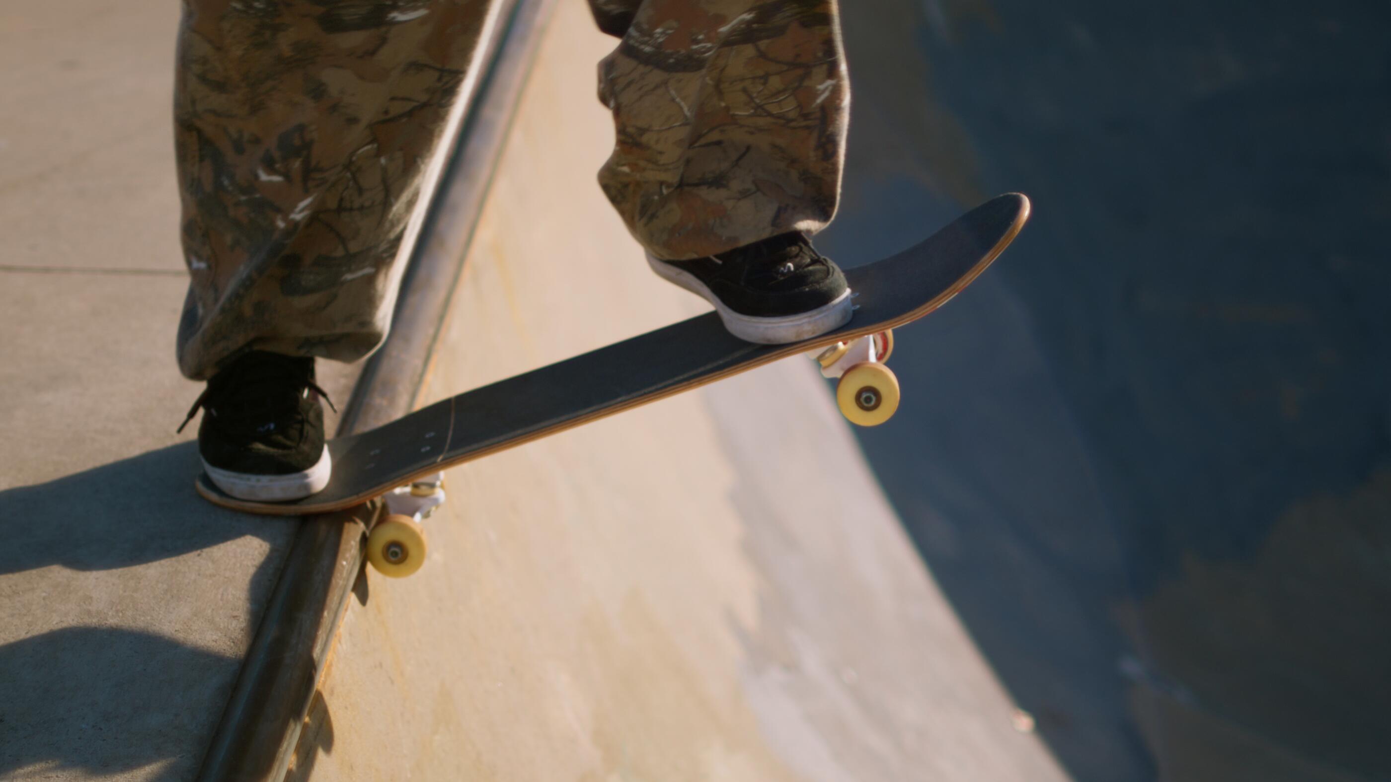 Male skateboarder dropping in on a ramp at a sunny outdoor skatepark.