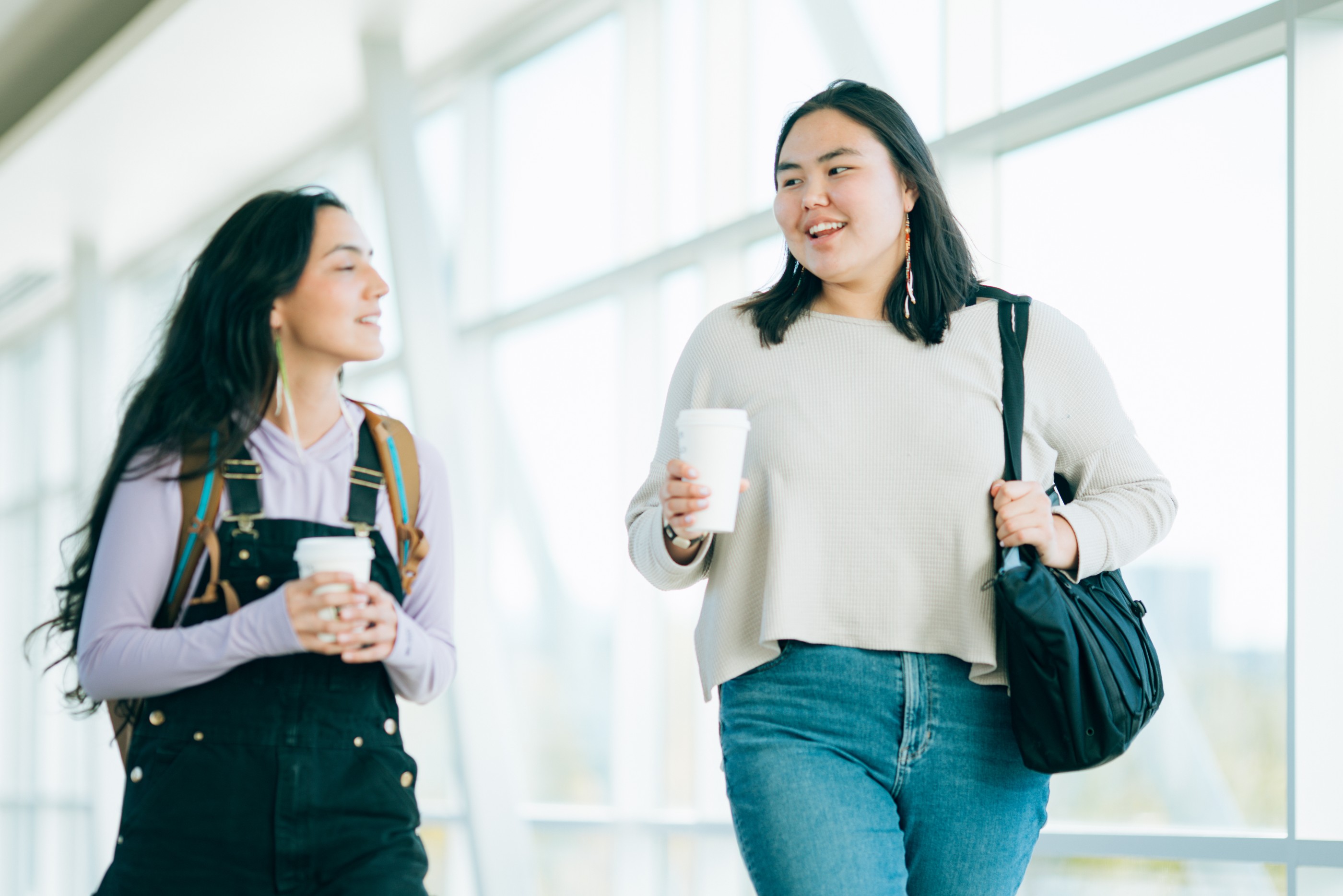 Two Indigenous Alaskan woman at University walk and talk down a campus hallway between classes.  Shot in Anchorage, Alaska, USA.