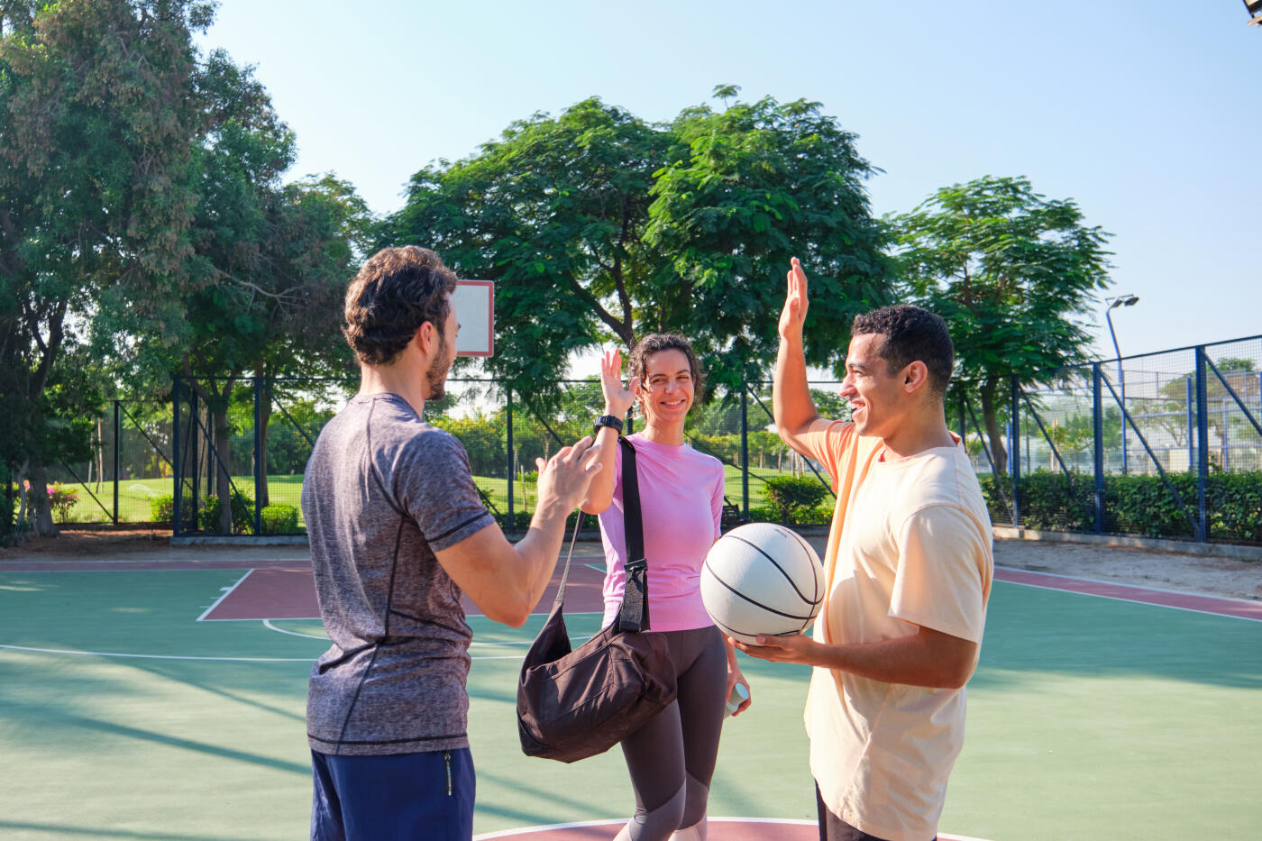 Multiracial people greeting each other. Male and female friends are giving high-five. They are standing in basketball court.