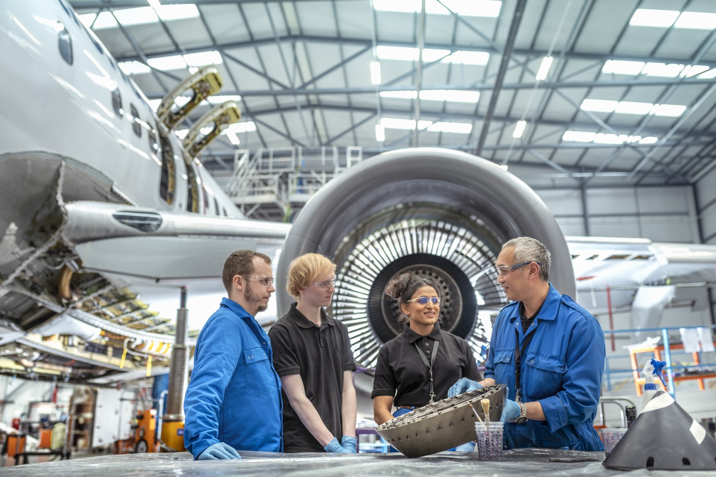 Aircraft engineer instructing apprentice engineers in front of jet engine in aircraft maintenance factory