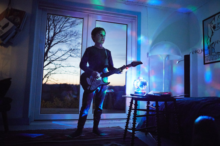 Boy playing electric guitar in living room with neon light