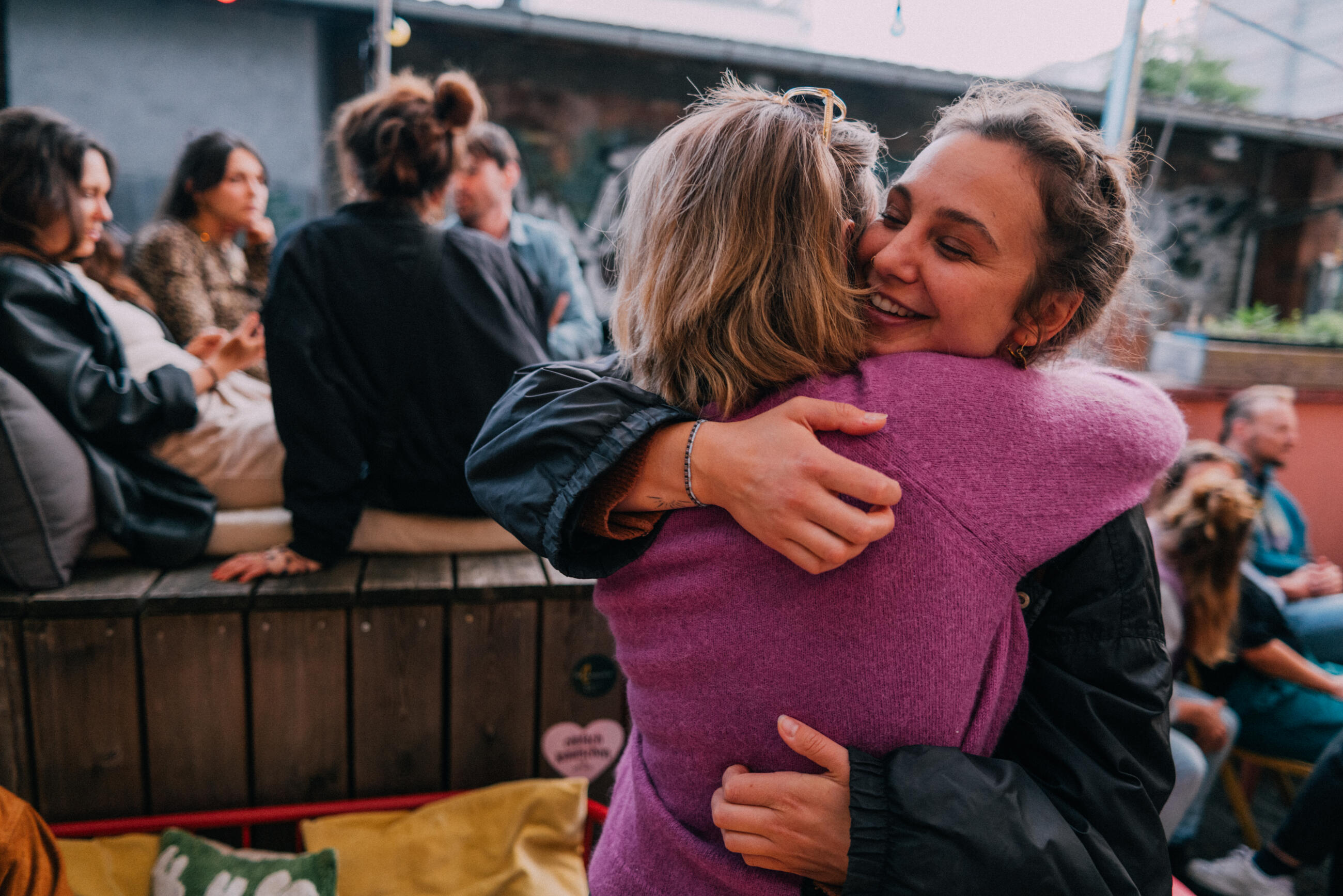 Two Female Friends Embracing Warmly at a Social Gathering Outdoors