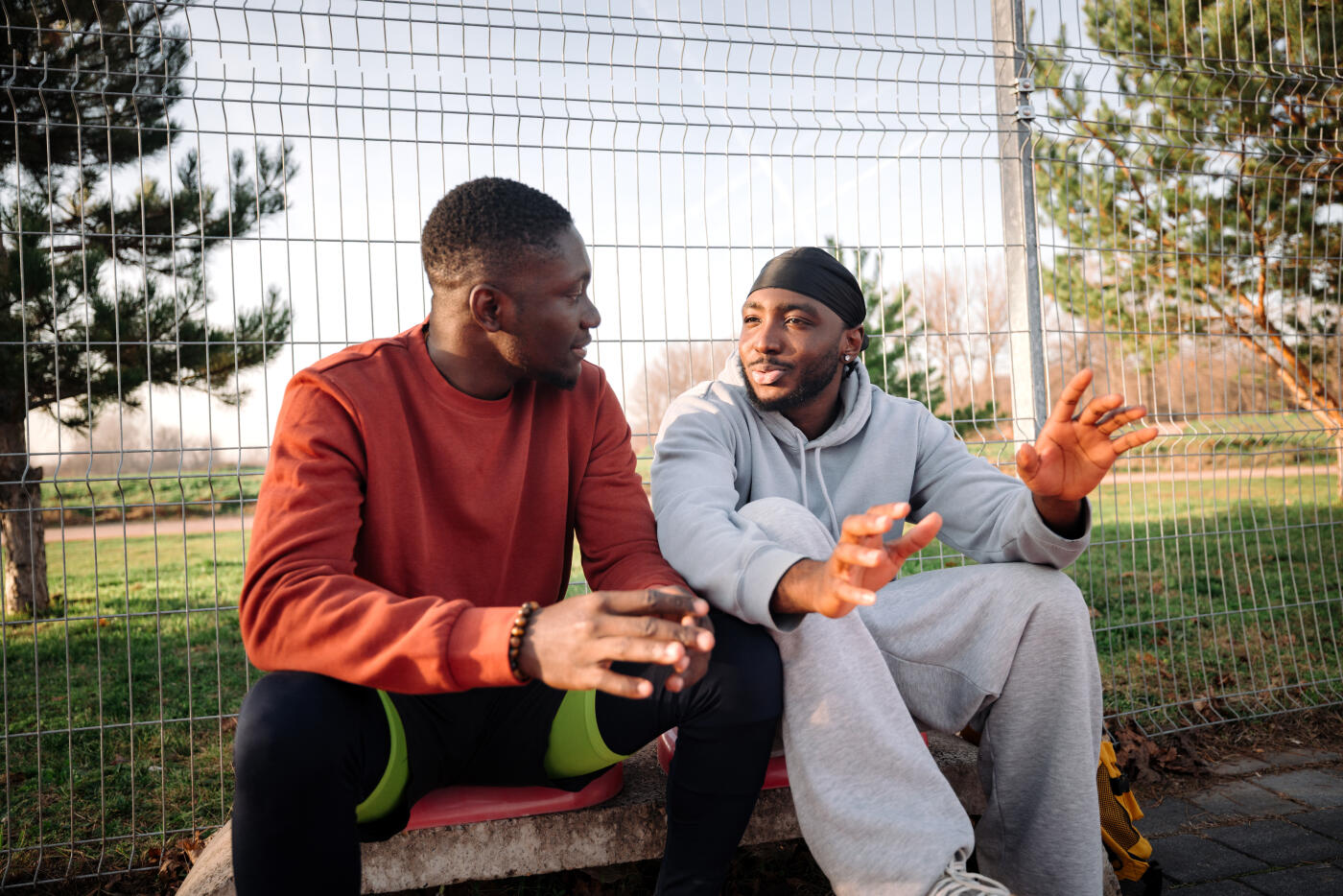 Two male friends sitting on bench and talking on outdoor sports court