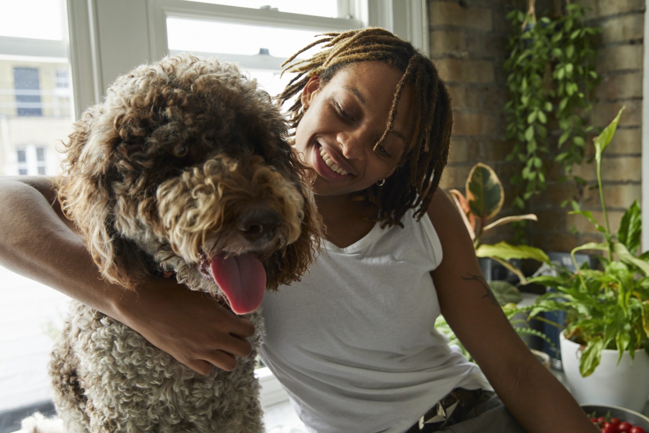 Close up shot of a multiracial person smiling with their arm around a labradoodle