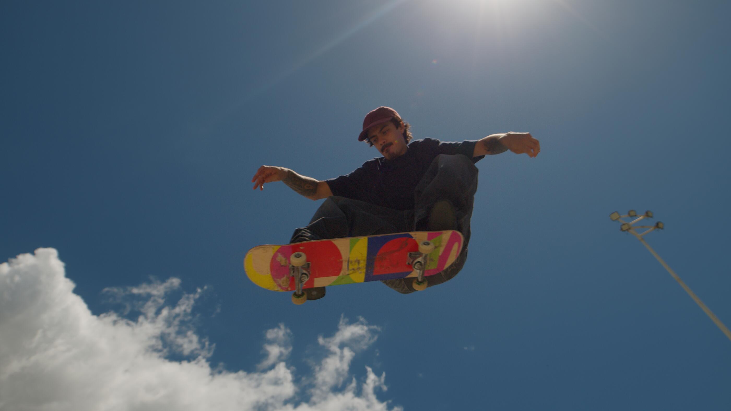 Male skateboarder performing a trick at a sunny outdoor skatepark.