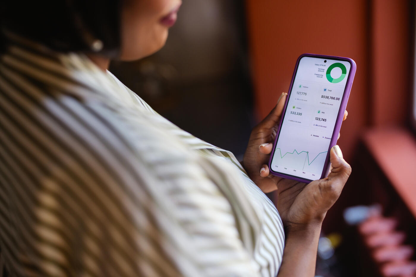 Close-up of a woman holding a smartphone displaying financial statistics and data, representing business, finance, and technology.