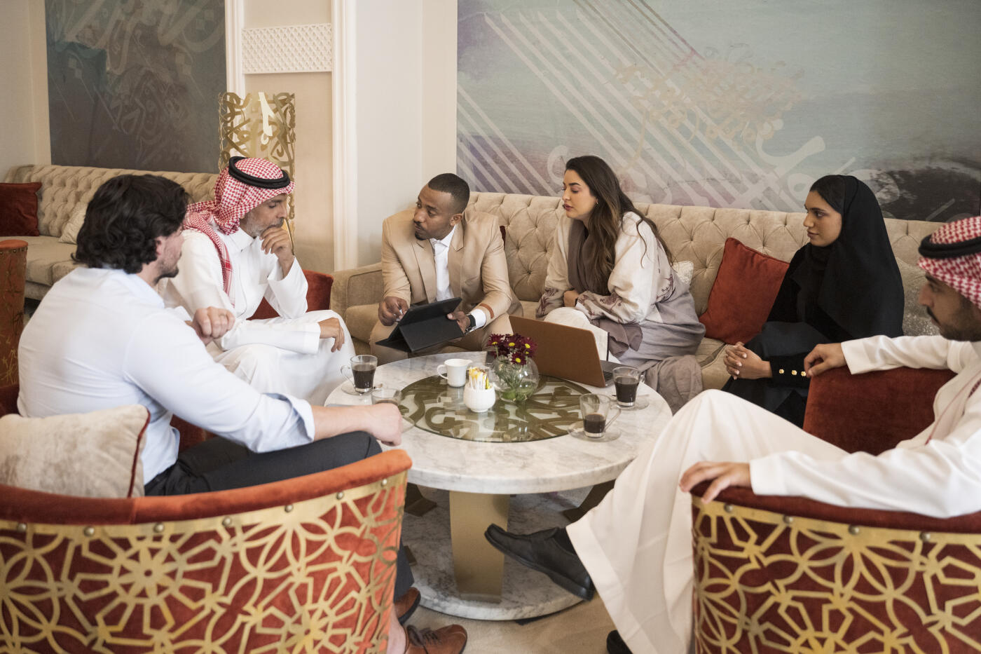 Middle Eastern professionals in 20s and 30s sitting around table in elegant tea lounge and sharing ideas with mature project manager.