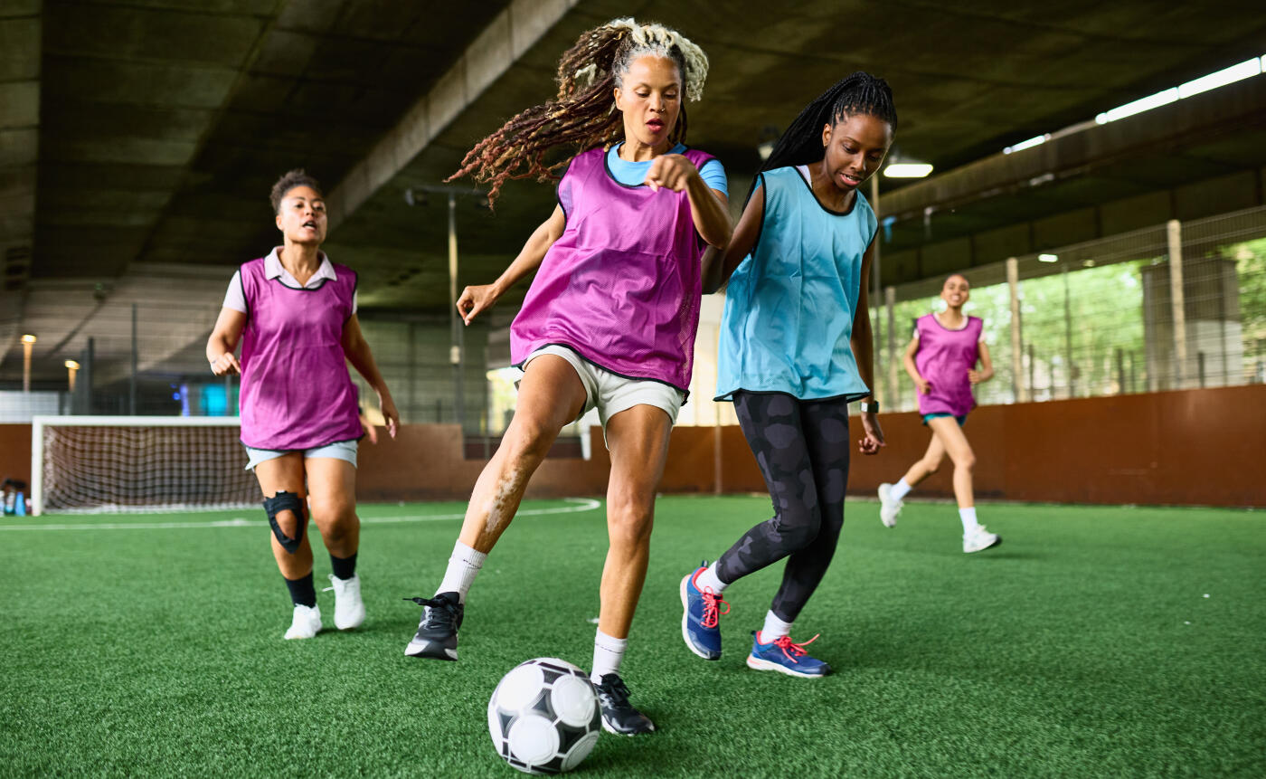 Female five a side soccer players playing game on astro turf beneath flyover in the city, community, skill