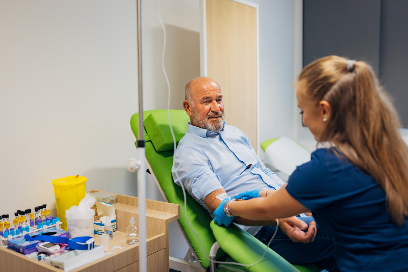Preparation for blood test with senior man by female doctor in medical uniform in clinic ordination room. Female doctor pierces the patient's arm vein with needle tube