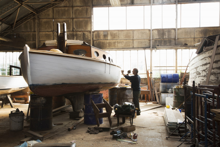 Skilled craftsman reconditioning old sailing boats in boat yard near Norfolk Broads UK.