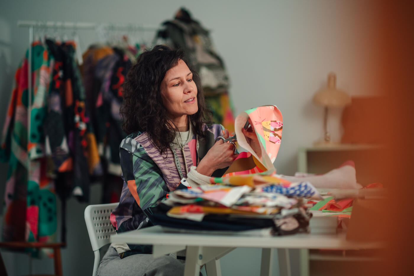 Female fashion designer cutting fabric with scissors, creating new clothing designs in her bright, artistic workshop