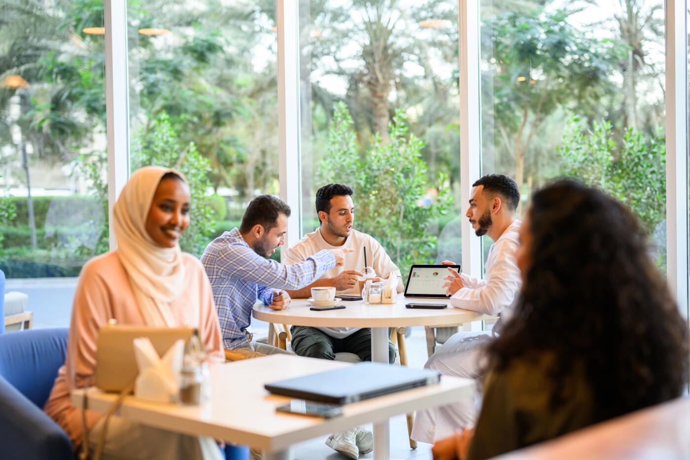 Side view of a small group of Middle Eastern professionals engaging in cheerful business meetings and discussions at their tables. Collaboration and connection in a cafe.