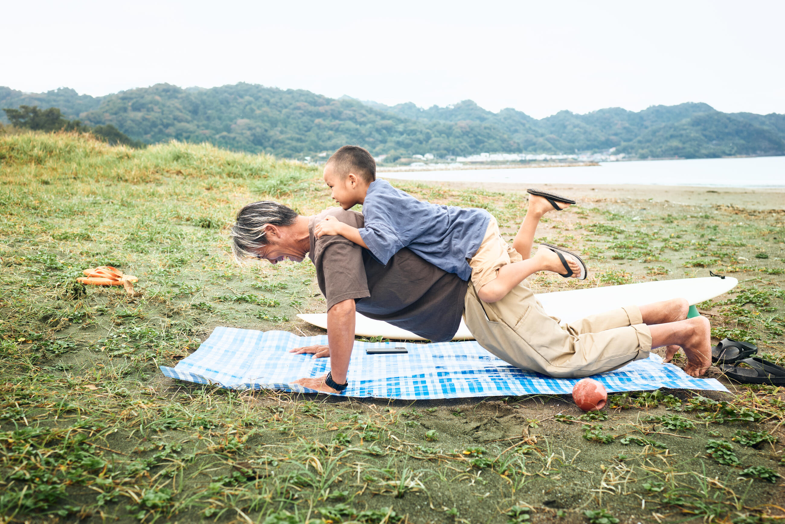Son rides on his father's back as he does push-ups on the beach.