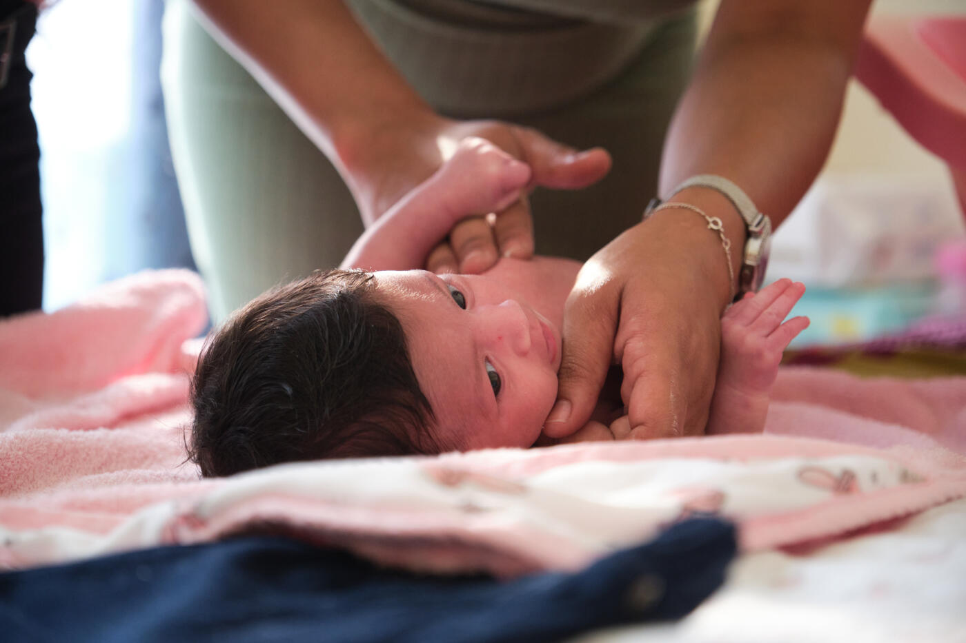 Mother massaging newborn baby after bath at home. Cute little girl is being taken care. She is looking away while lying down on bed.