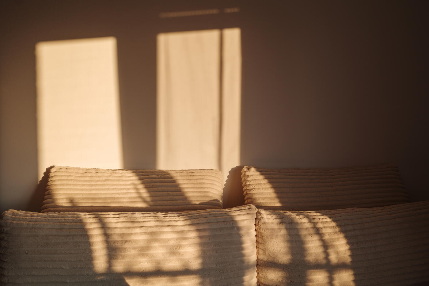 Soft golden sunlight filters through a window, casting long, gentle shadows on a plush, textured sofa.