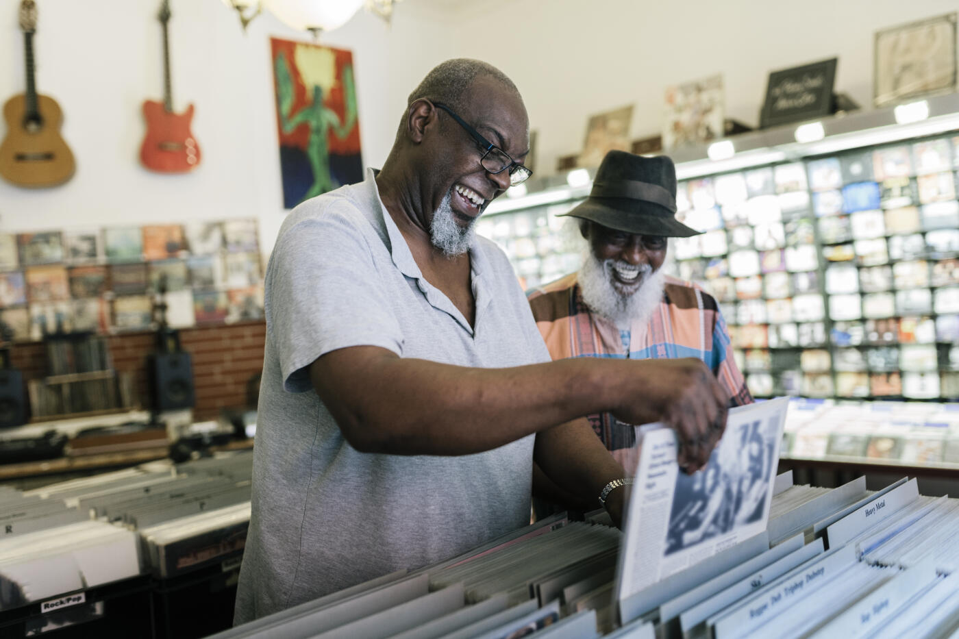 Two elderly black male friends searching record bins in a record store.