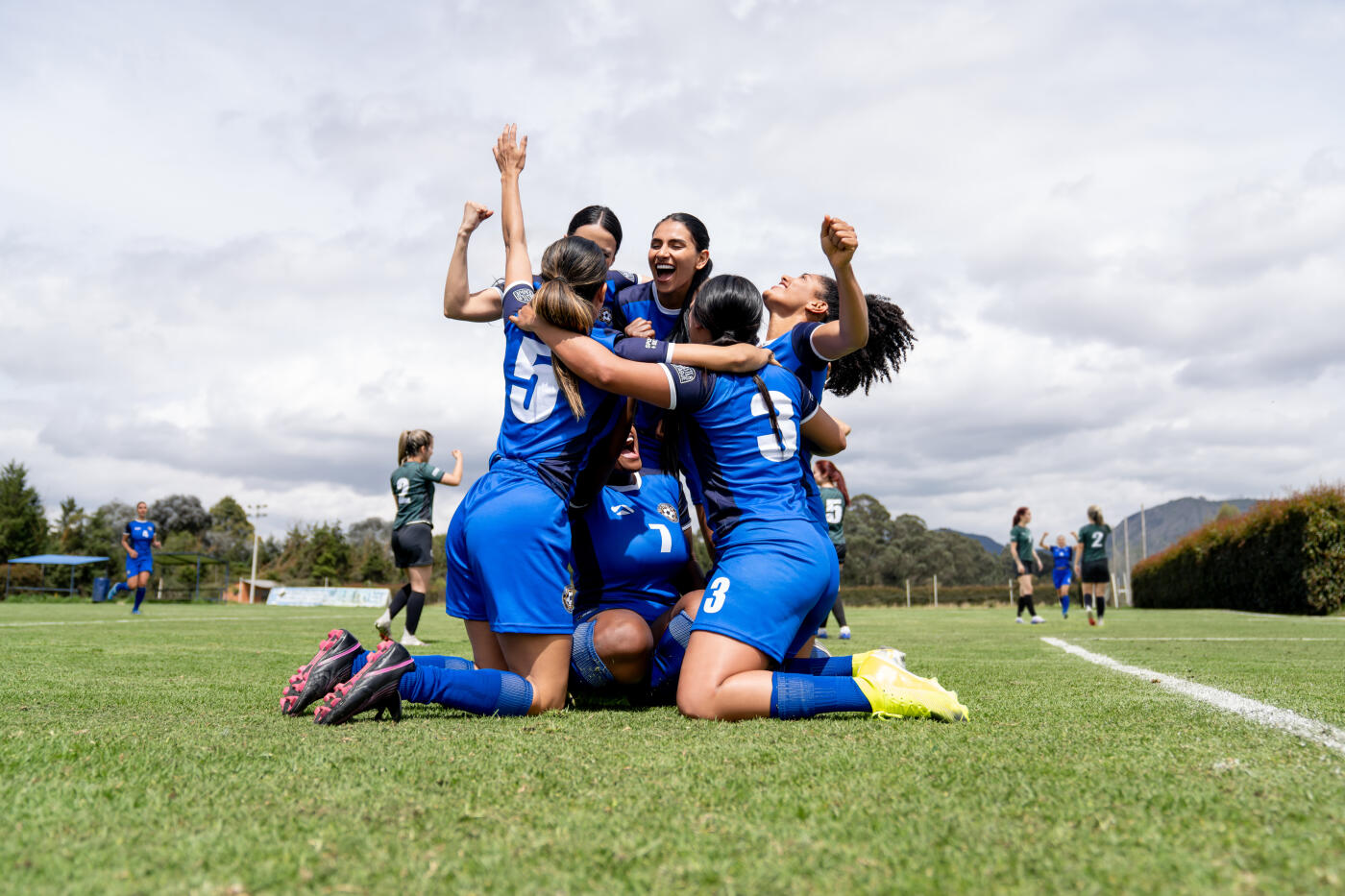 Excited female soccer team celebrating a goal in the field and smiling - sports concepts