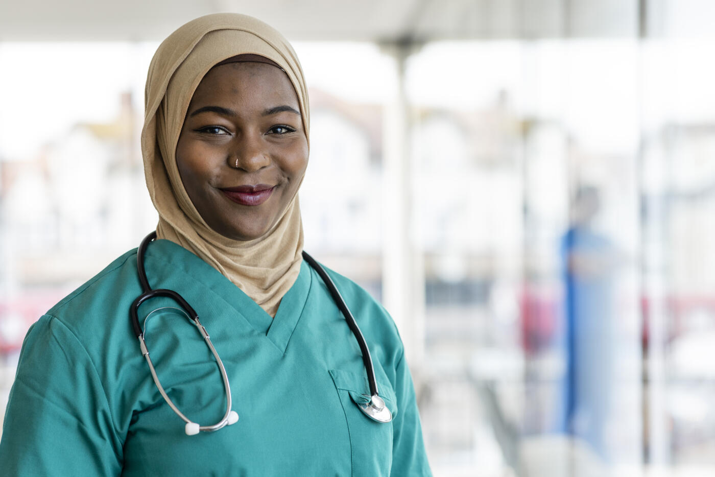 Portrait of a medical professional working in a hospital in the North East of England. She is dressed in scrubs with a stethoscope around her neck looking at the camera smiling.