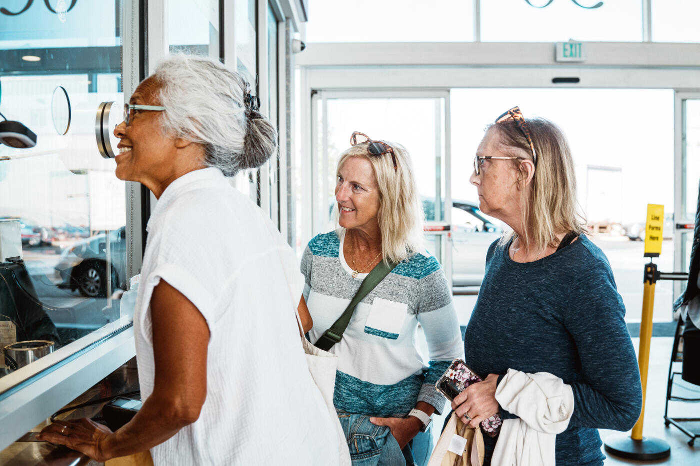 A multiracial senior woman of Hawaiian and Chinese descent buys ferry tickets at a harbor ticket counter in Portland, Maine, while her friends wait nearby before heading to dinner on a nearby island.