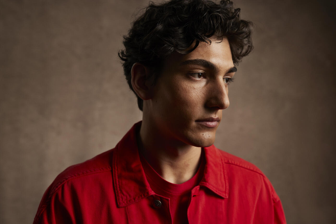 Headshot of contemplative young man in red casuals against brown background