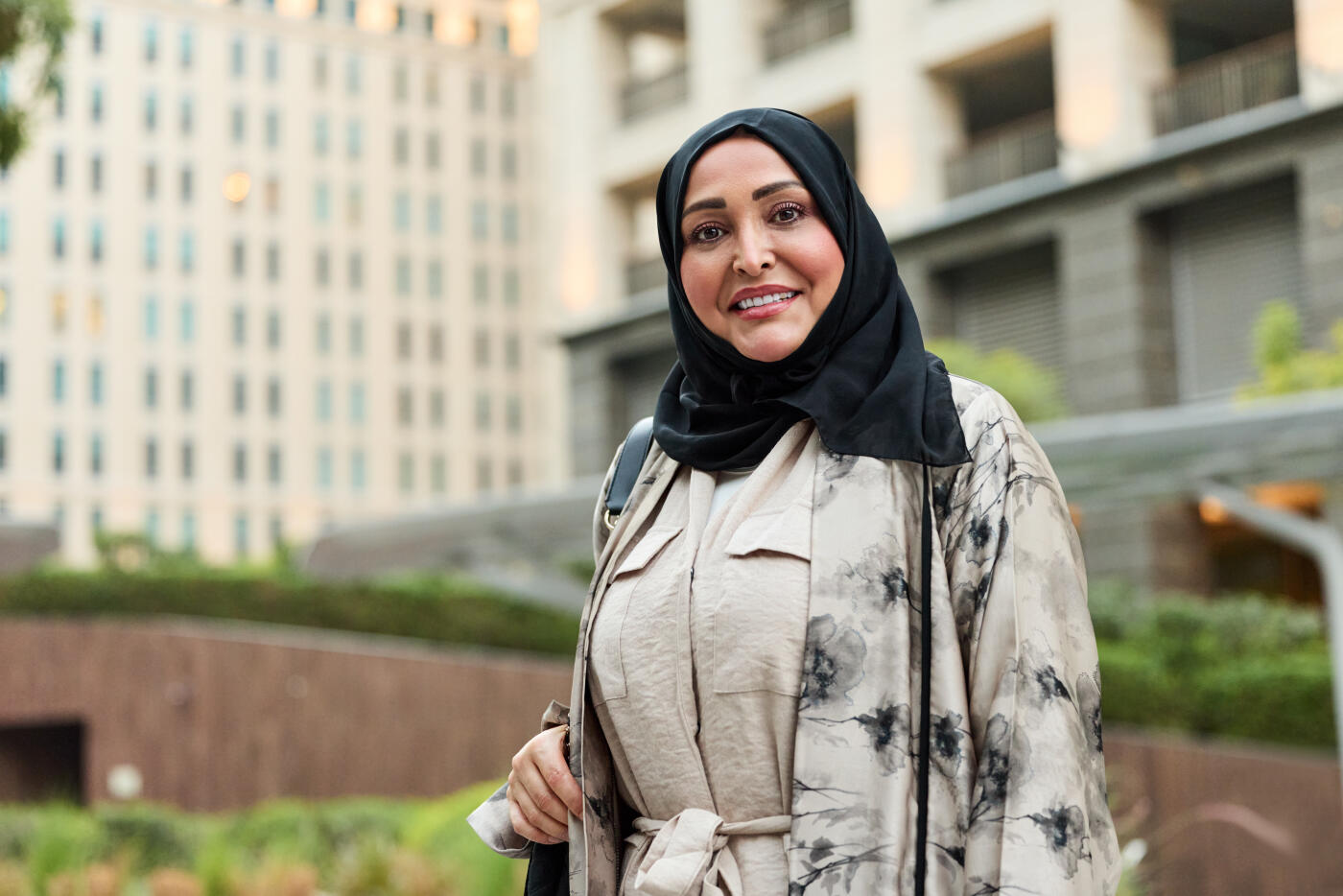 Portrait of smiling Emirati woman posing in city. Middle eastern female is She is wearing hijab paired with floral-patterned abaya. She is looking confidently at camera.