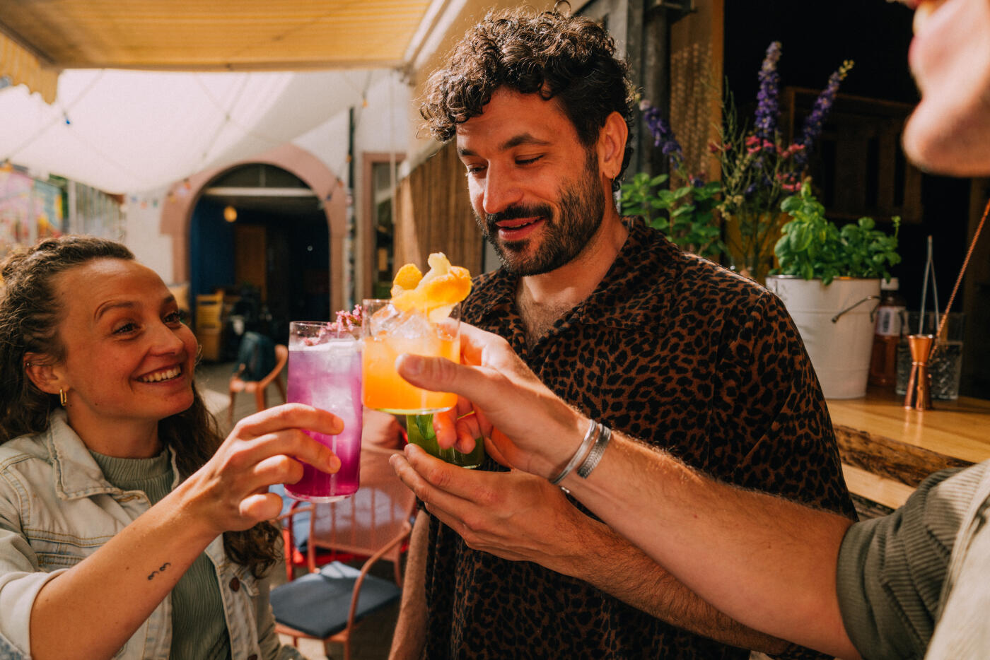 A joyful group of friends clinking glasses filled with vibrant drinks, celebrating at an outdoor venue. The scene captures friendship, happiness, and celebration during a cheerful social occasion. Part of a series with video