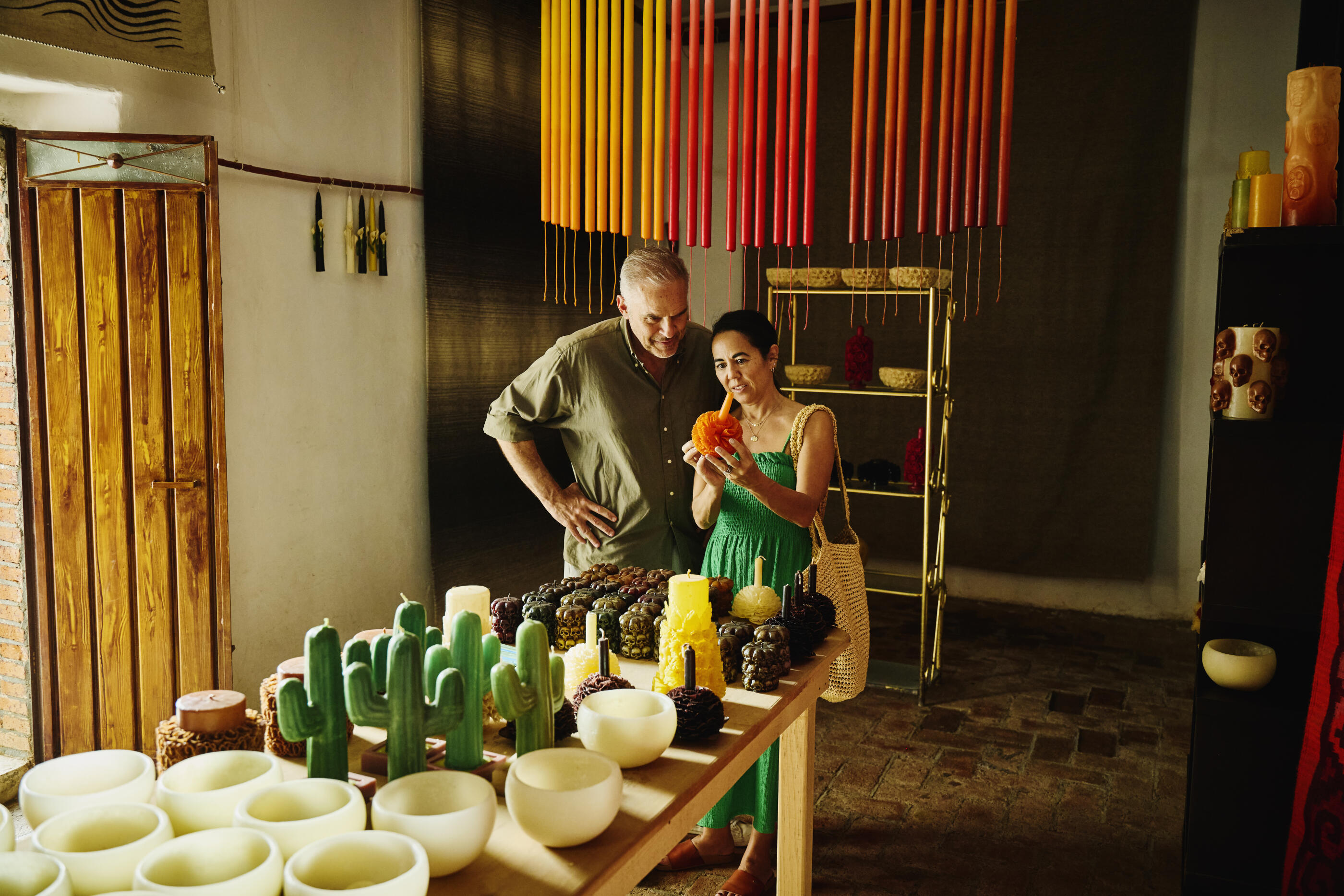 Wide shot of senior couple shopping and examining orange flower candle in traditional Oaxacan candle shop