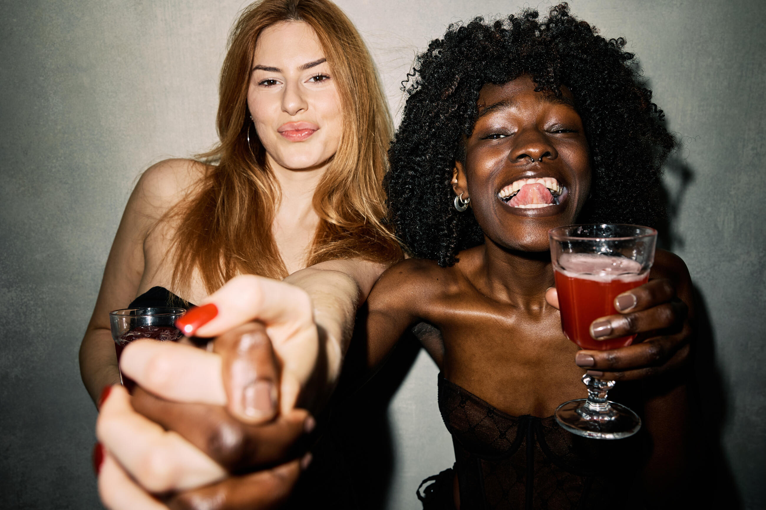 Two diverse young women laughing and holding cocktails on a lively night out, celebrating friendship and fun in a fashionable, multicultural urban party scene