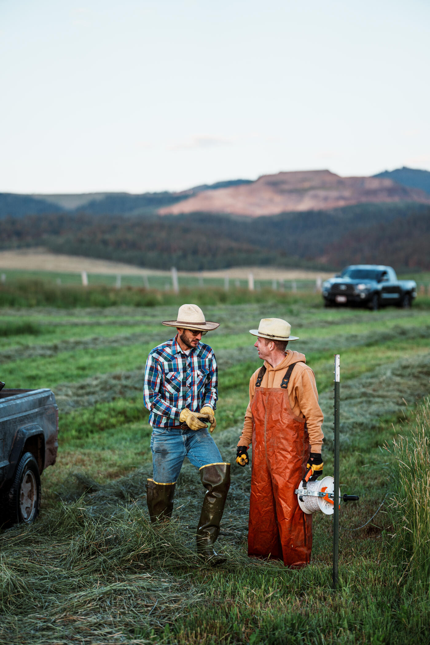 At sunrise, two ranchers discuss plans for installing a new electric fence in a dew-covered hay field in Western Wyoming.