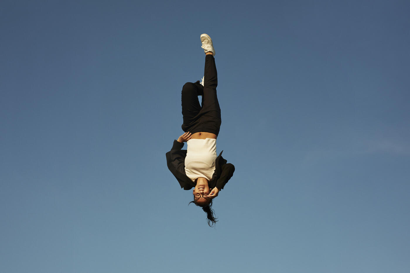 Smiling young woman with hand on hip levitating upside down against clear blue sky