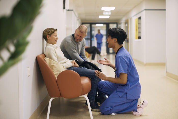 Happy young doctor explaining patient sitting next to father in corridor