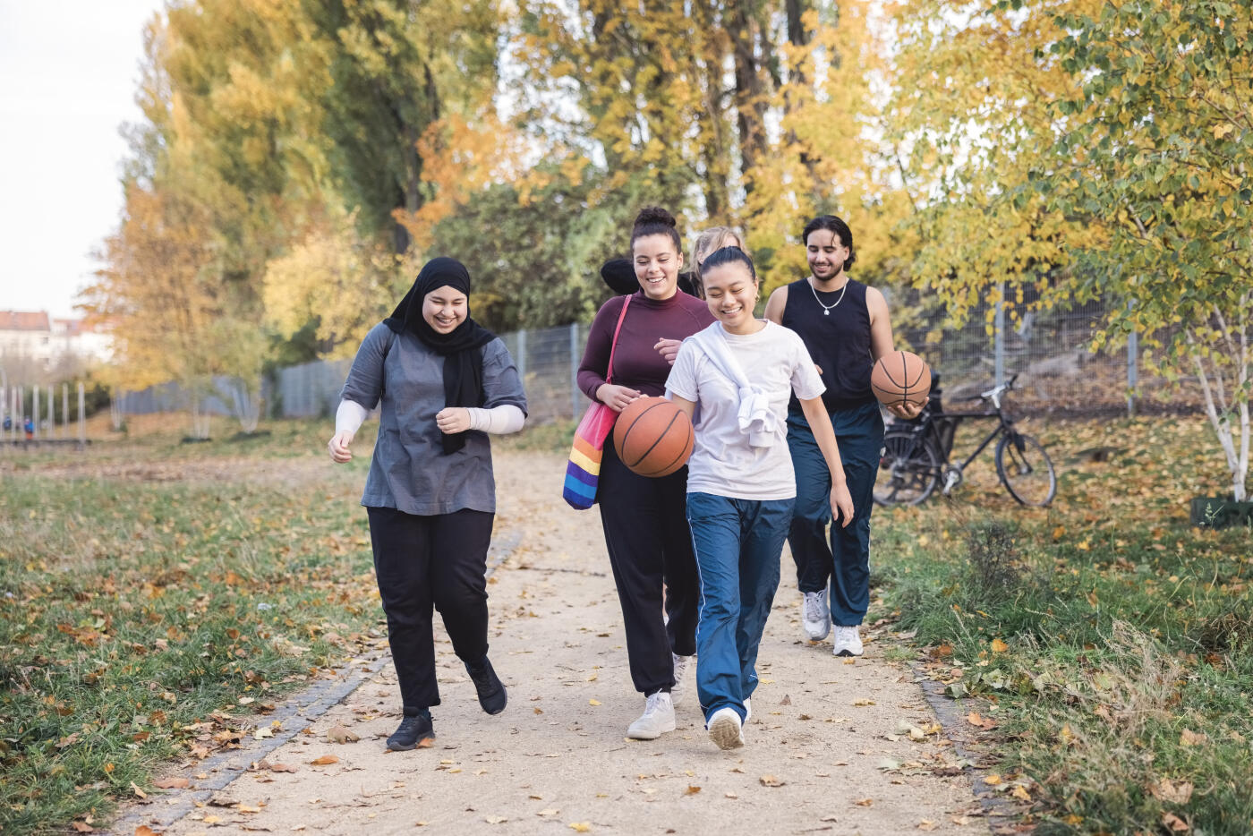 Multiracial group of people enjoying a walk outdoors with a basketball. Young friends walking together and smiling on pathway.