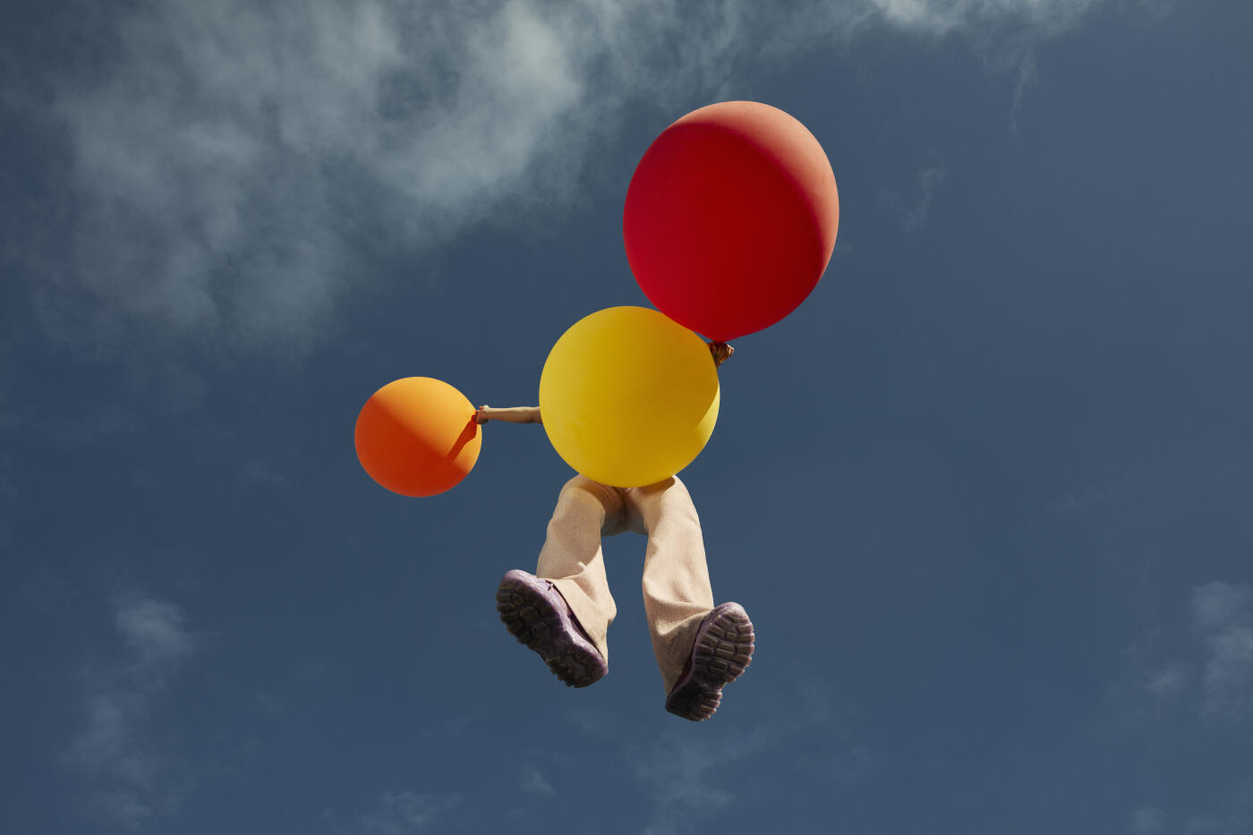 Directly below view of young woman with balloons flying high up against blue sky
